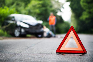 <p>A close up of a red emergency triangle on the road in front of a damaged car and unrecognizable people. A car accident concept. Copy space.</p>
